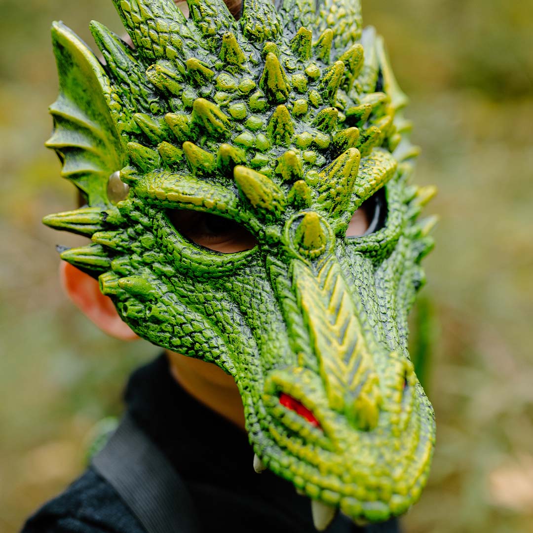 Detailopname van een kind dat een groen drakenmasker draagt, met de ogen zichtbaar door de openingen.