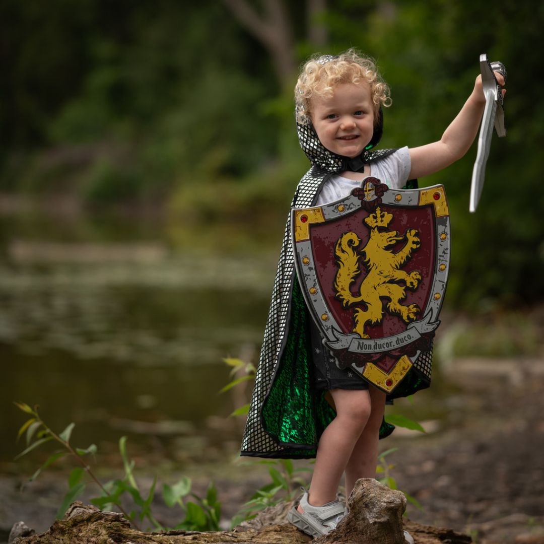 Een kind draagt de zilveren ridderkant van de Great Pretenders verkleedcape met een schild en zwaard.
