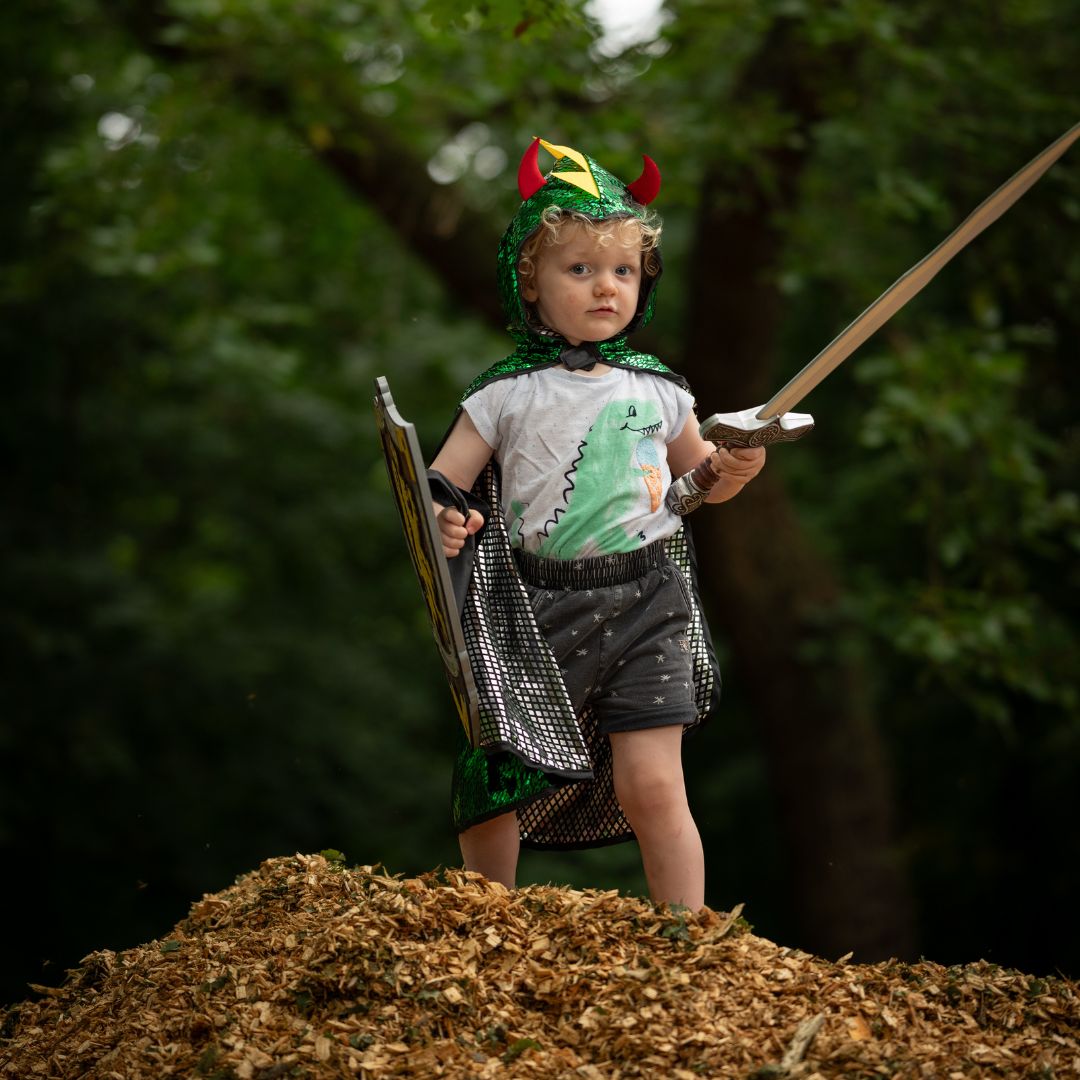 Een kind draagt de groene drakenkant van de Great Pretenders verkleedcape met hoorns op de capuchon en een zwaard.