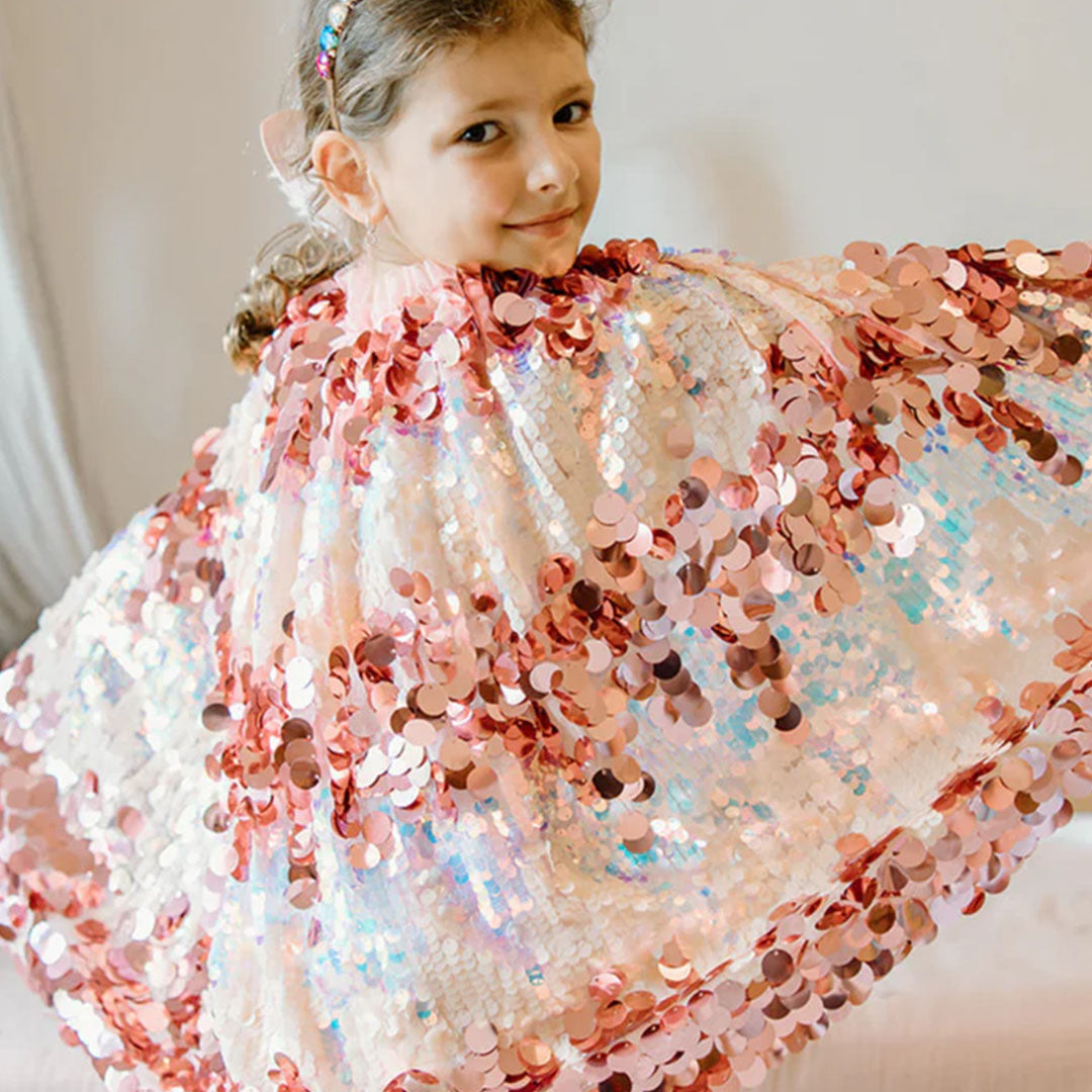 Een meisje draagt de roze verkleedcape met pailletten, die wijd uitgespreid is.