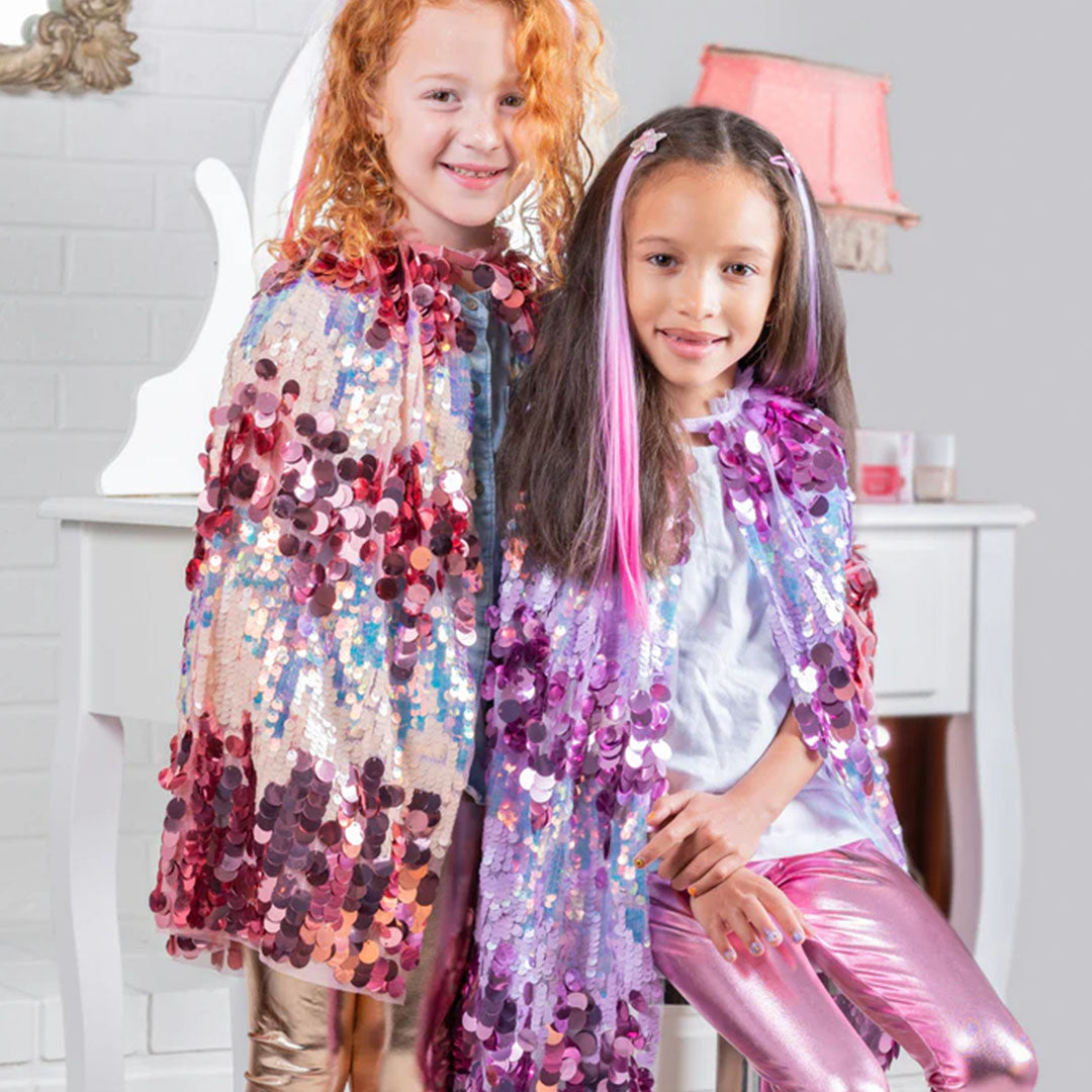 Twee lachende meisjes dragen een roze en een paarse verkleedcape met pailletten.