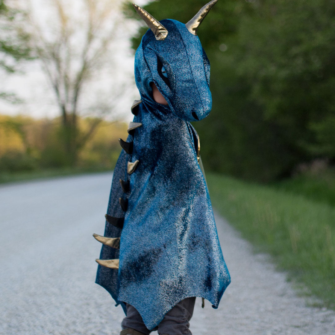 Kind van achteren gezien, draagt de blauwe Great Pretenders draken verkleedcape met gouden stekels op de rug, buiten op een pad.