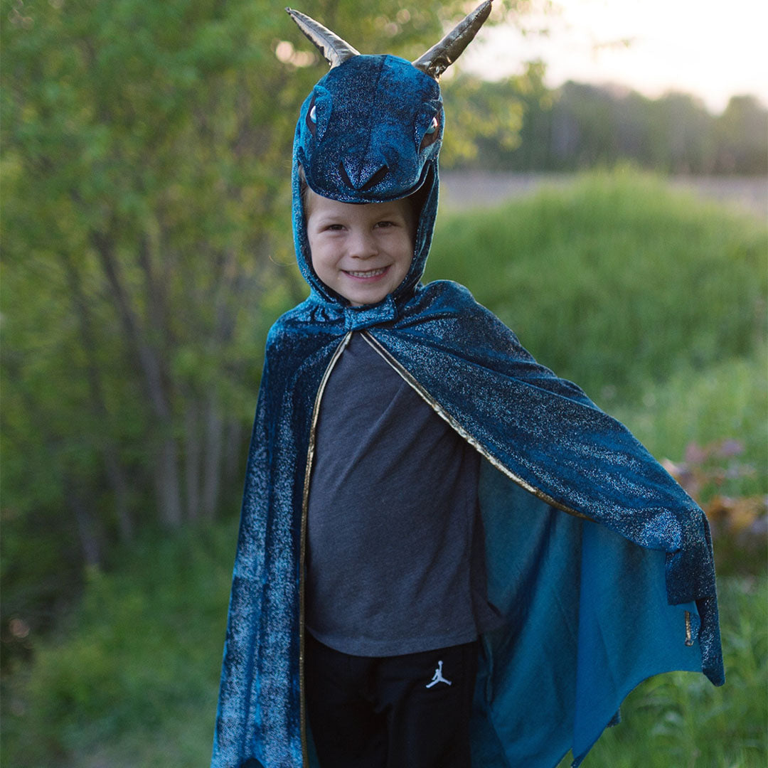 Lachend kind draagt de open blauwe Great Pretenders draken verkleedcape met gouden rits, buiten in het groen.