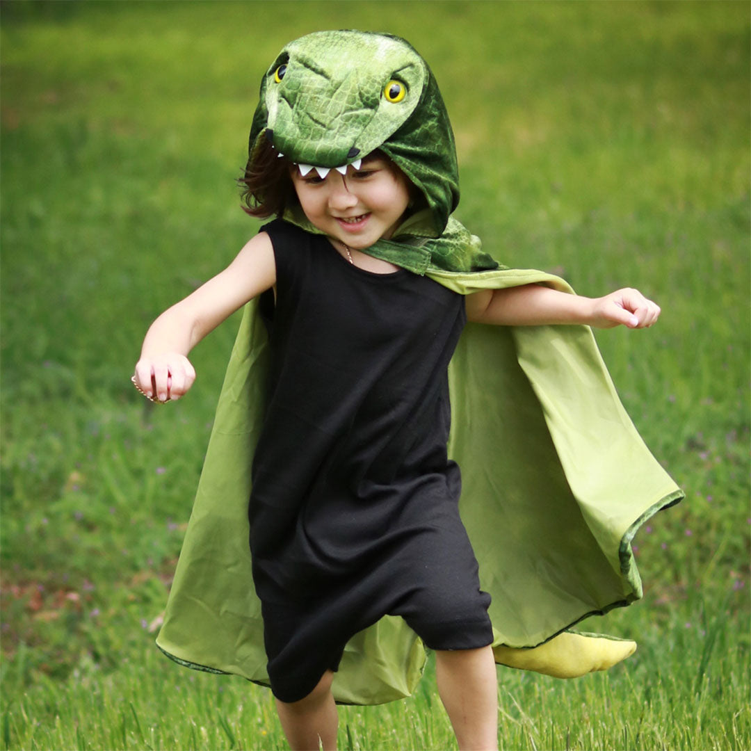 Een kind rent in het gras, gekleed in de groene dino T-Rex verkleedcape.