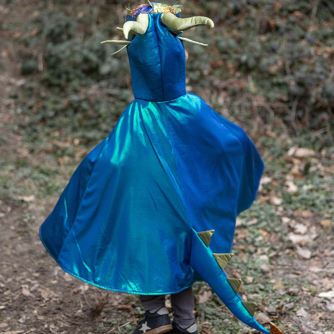 Kind van achteren gezien in een Great Pretenders draken verkleedcape met blauwe cape en staart in een bos.