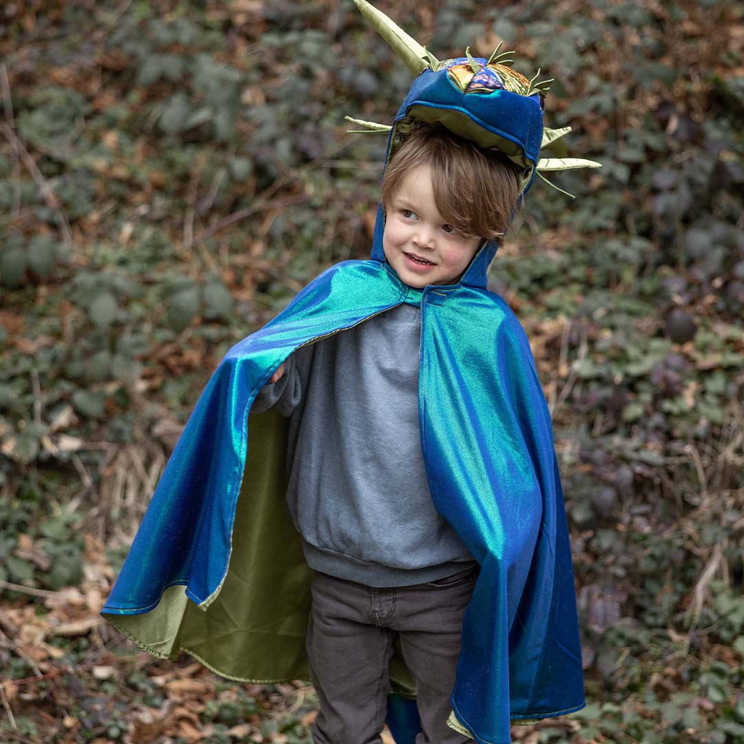 Een kind draagt de Great Pretenders verkleedcape draak emerald in een bosrijke omgeving.