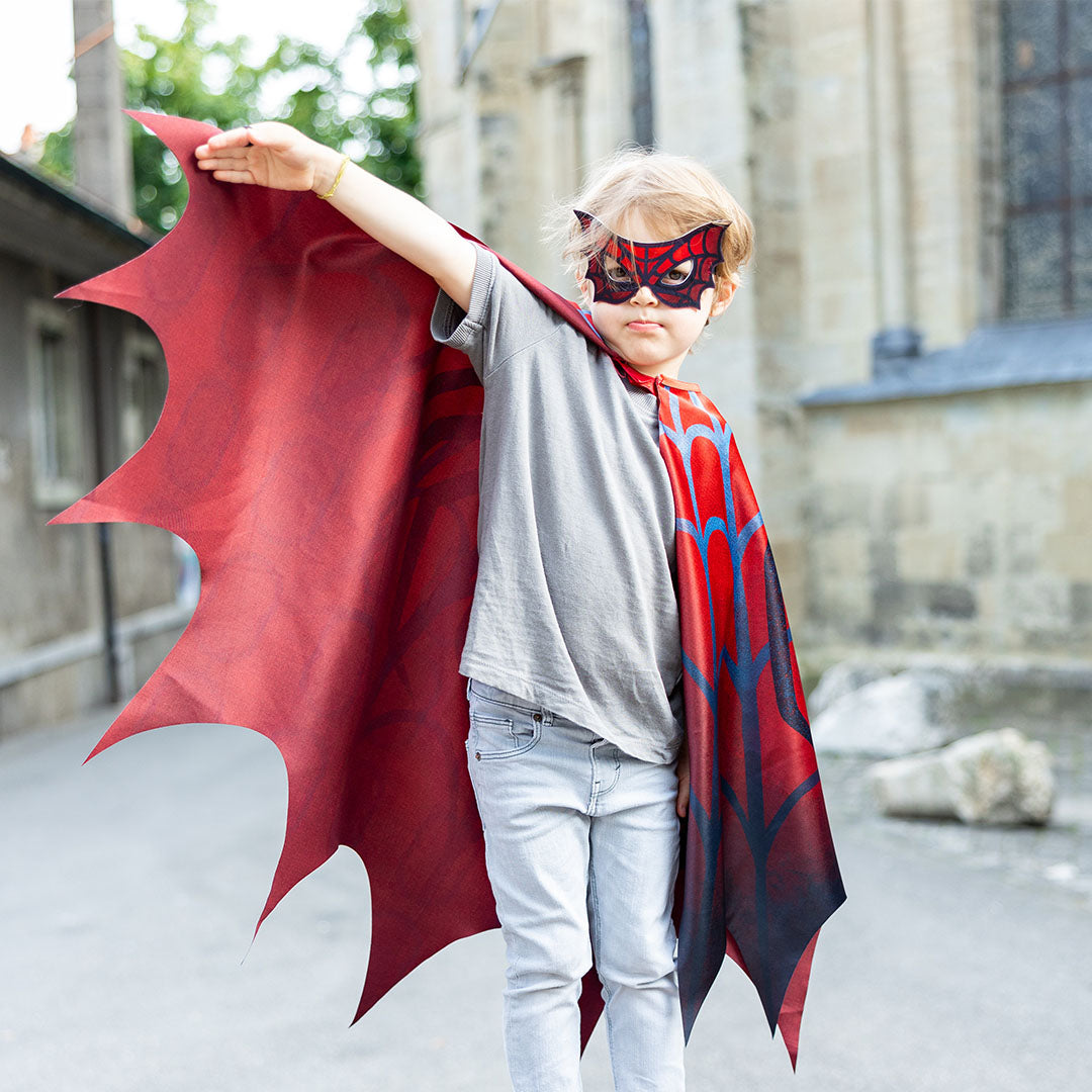 Een kind draagt de verkleedcape en masker webwever en poseert als superheld met een opgeheven arm.