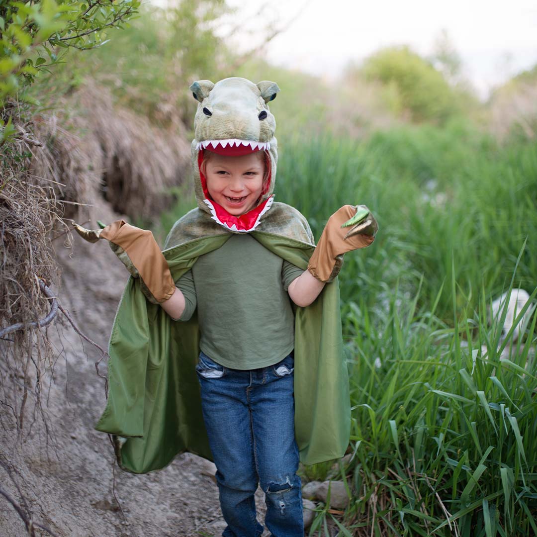 Lachend kind draagt de great pretenders T-Rex verkleedcape met klauwen in een groene omgeving.