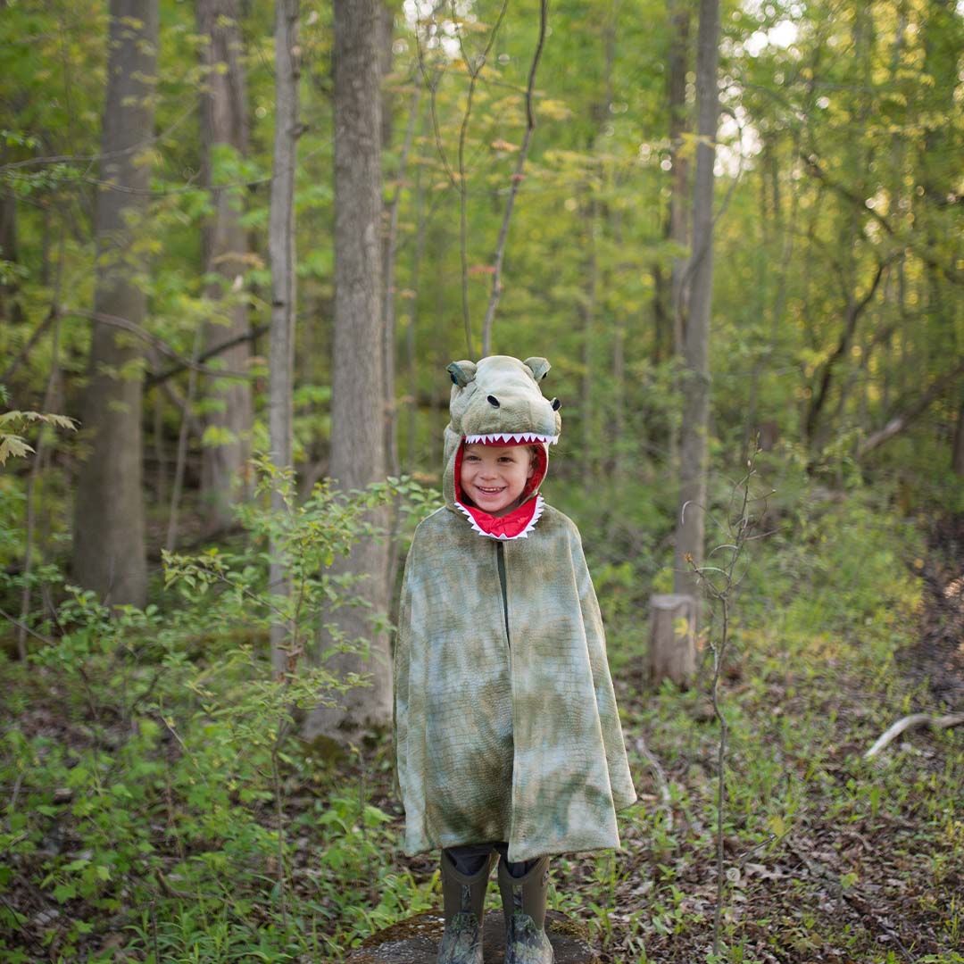 Kind draagt de great pretenders T-Rex verkleedcape met schubbenpatroon in een bos.