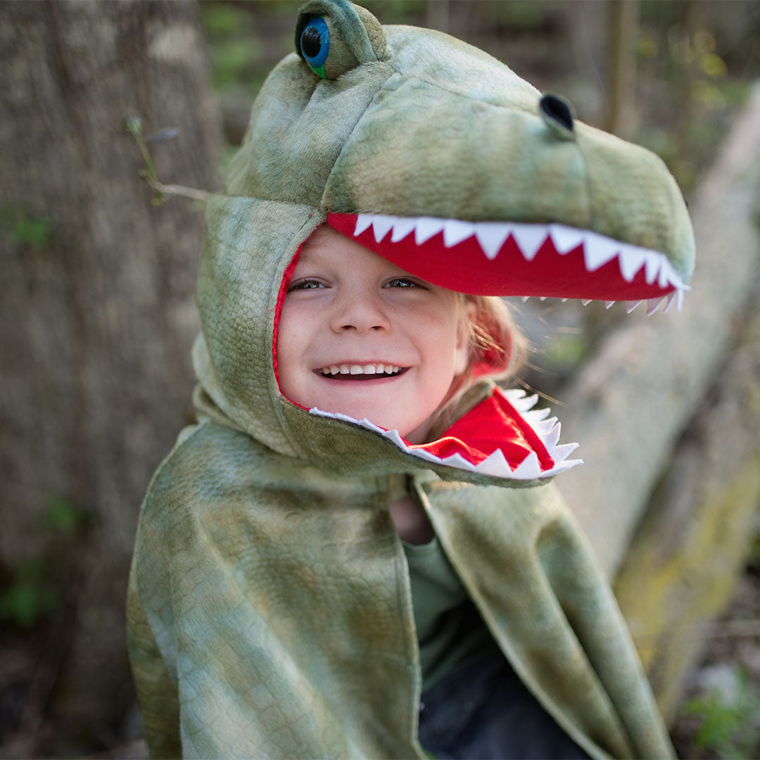 Close-up van een lachend kind in de great pretenders T-Rex verkleedcape, met het gezicht in de bek van de dinokap.