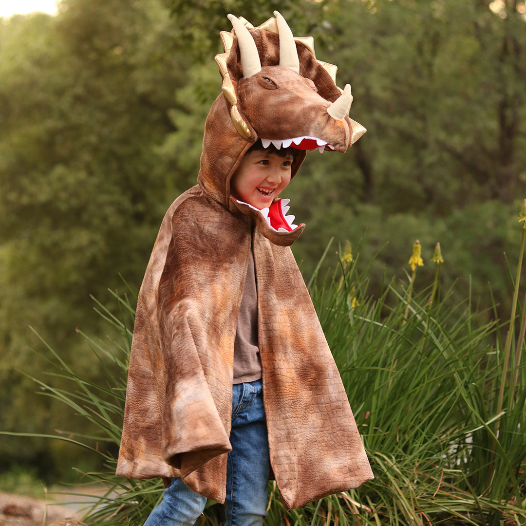 Een kind loopt met de triceratops verkleedcape aan in een groene buitenomgeving.