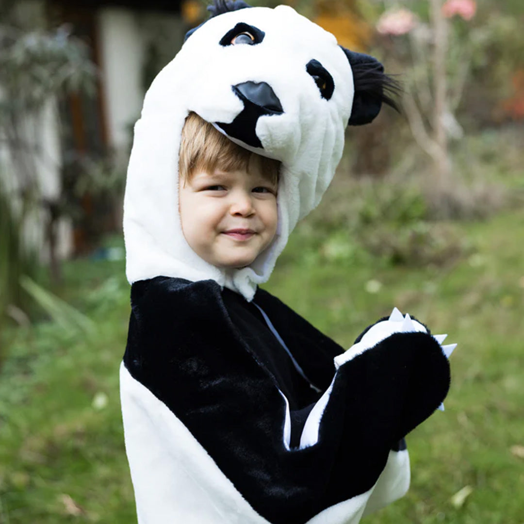Lachende peuter draagt de Great Pretenders panda verkleedcape en kijkt over de schouder in het gras.
