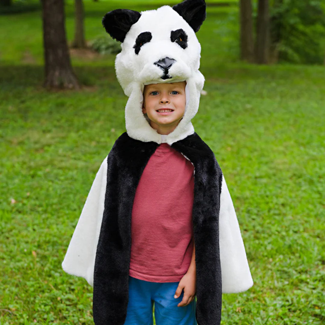 Peuter draagt de Great Pretenders panda verkleedcape en staat in een park met bomen en gras.