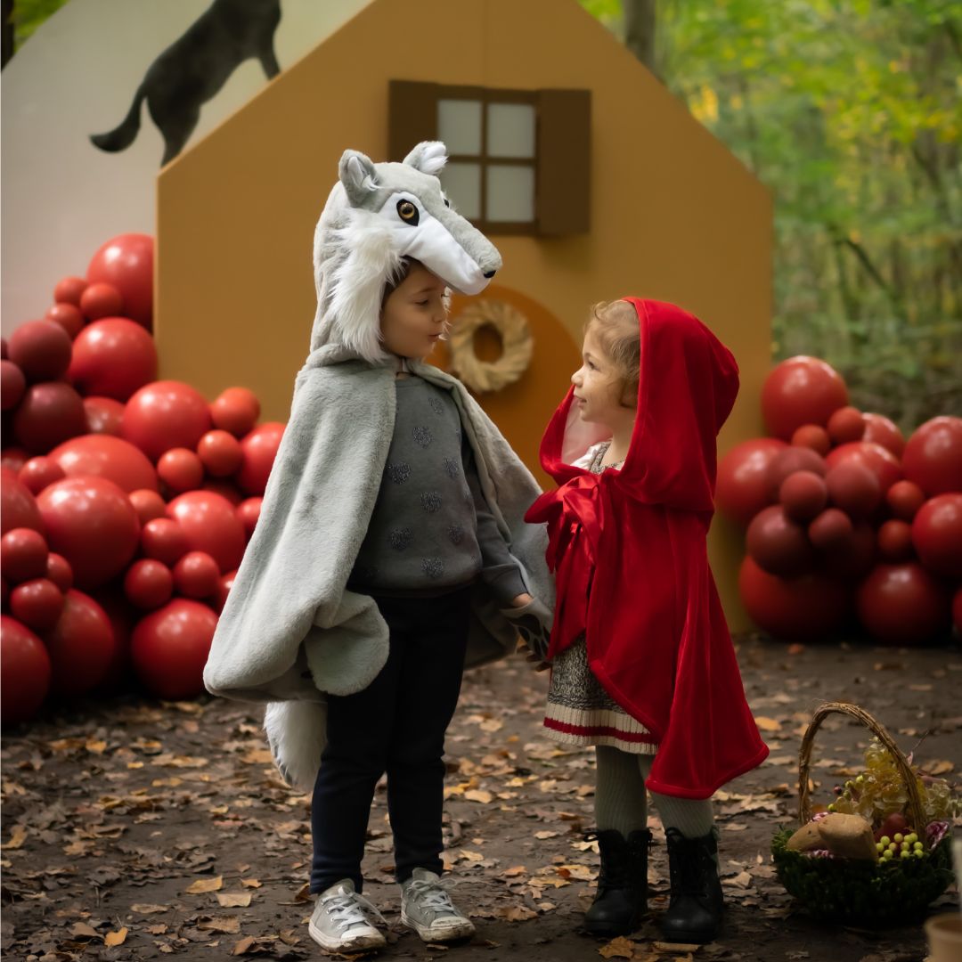 Twee kinderen, één als Roodkapje met de Great Pretenders cape en één als wolf, staan tegenover elkaar in een bos.