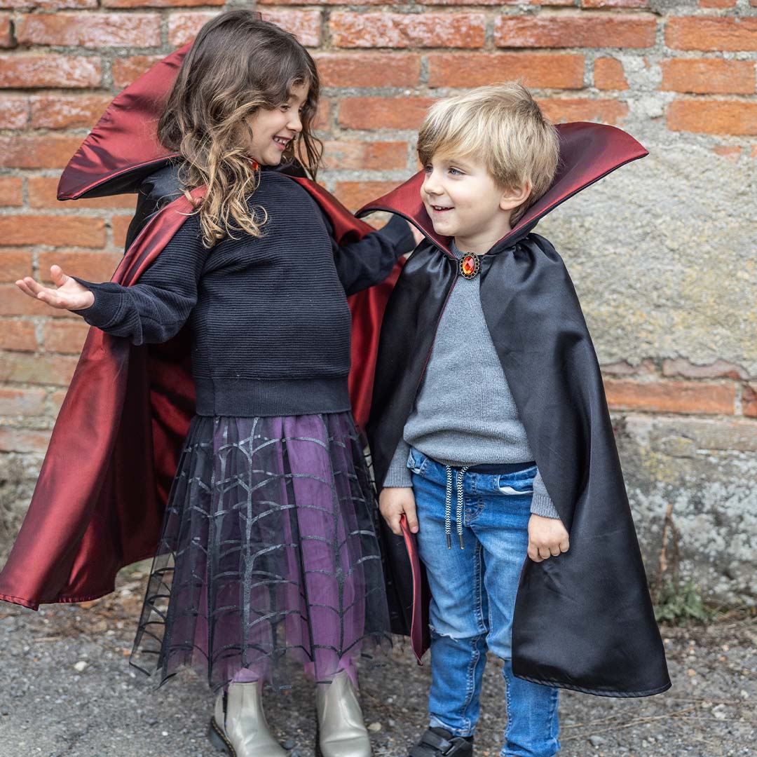Twee lachende kinderen dragen de zwarte en rode vampier verkleedcape voor kinderen.
