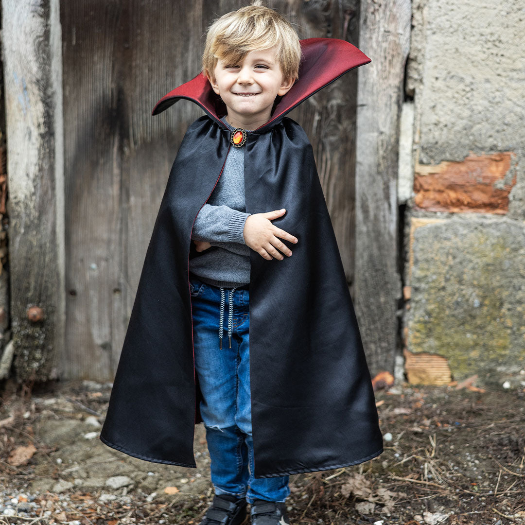 Een lachende jongen draagt de zwarte en rode vampier verkleedcape met een broche.