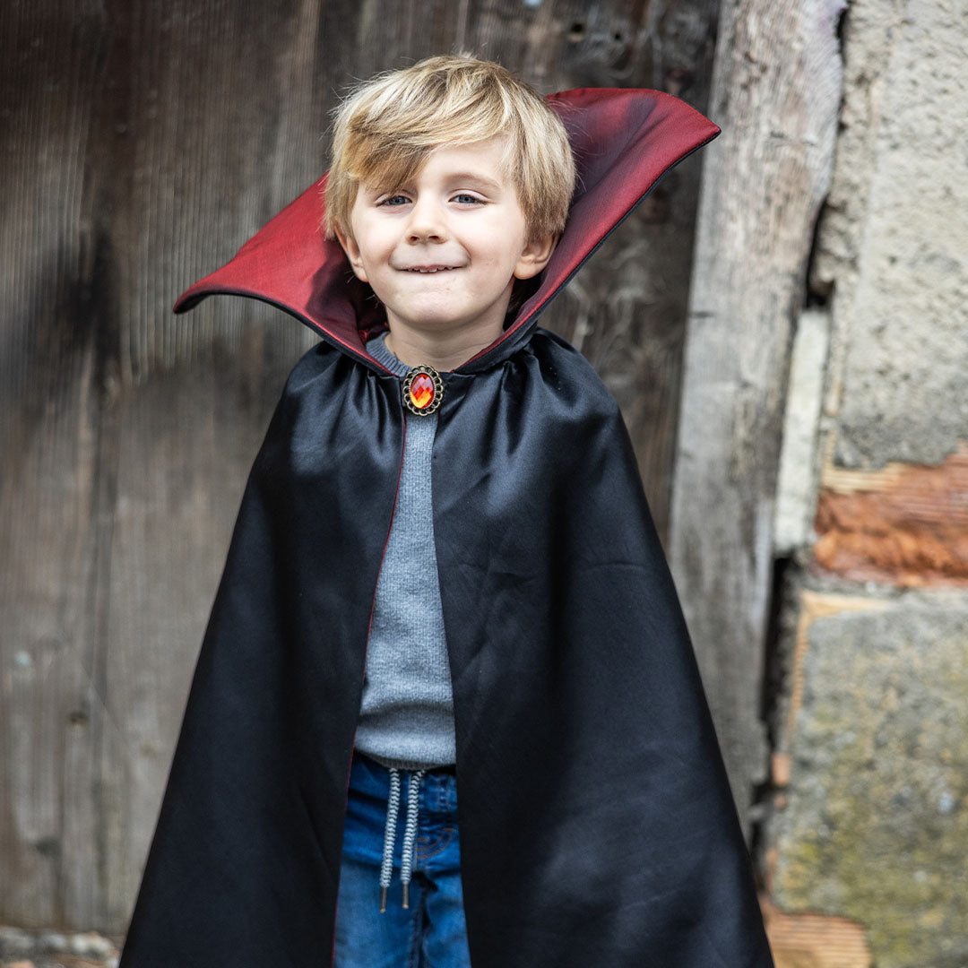 Een lachende jongen draagt de zwarte en rode vampier verkleedcape met een broche.