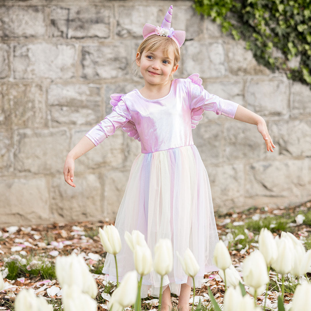 Meisje met eenhoorn verkleedjurk en diadeem staat lachend in een tuin met witte tulpen.