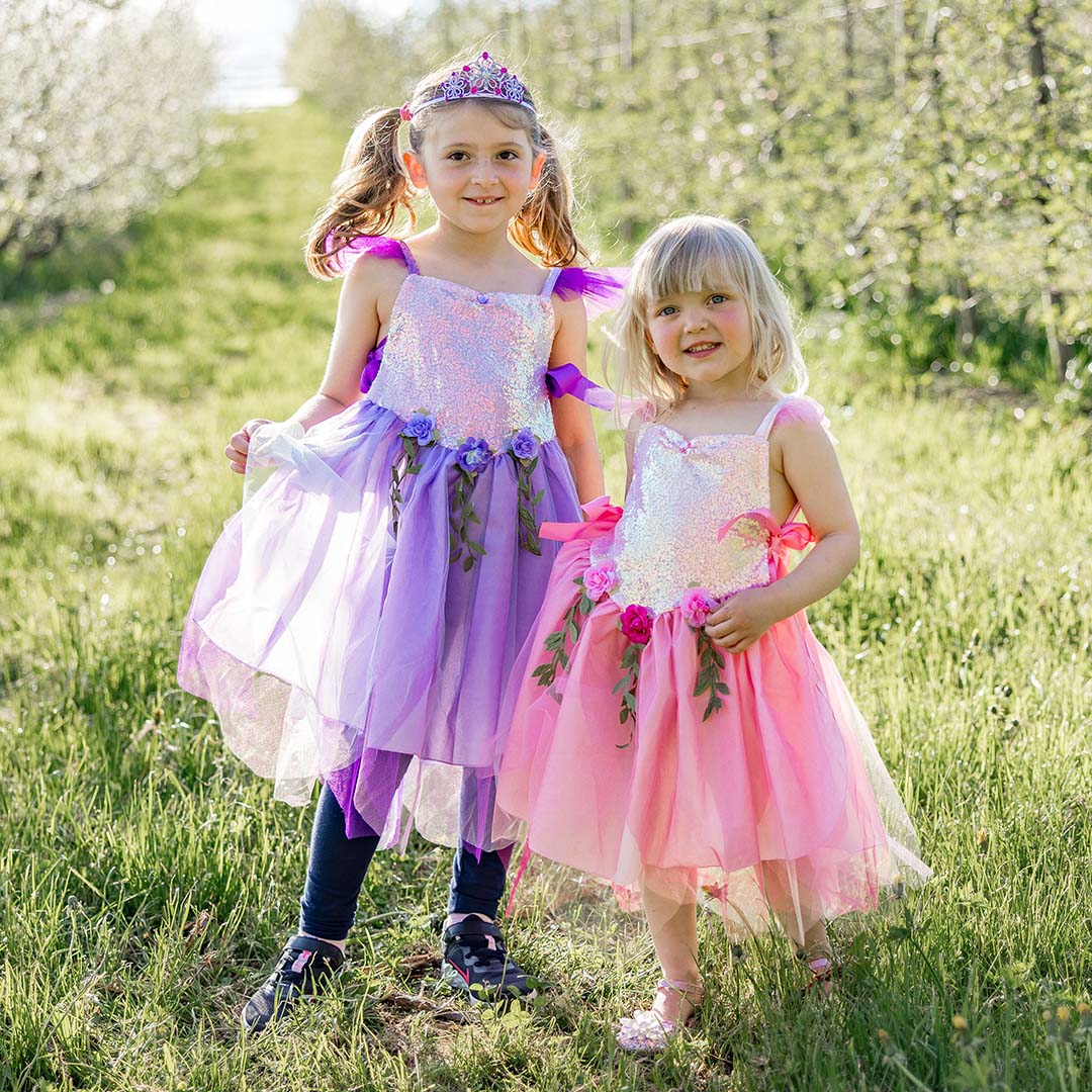 Twee meisjes dragen Great Pretenders sprookjes verkleedjurken, één roze en één paars, in een groen veld.