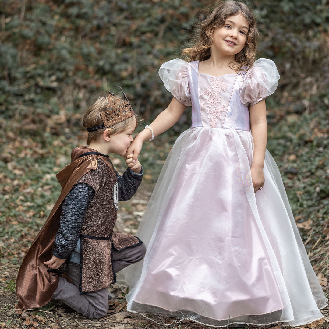 Een meisje in de roze prinsessen verkleedjurk met een jongen in ridderkostuum in een bos.
