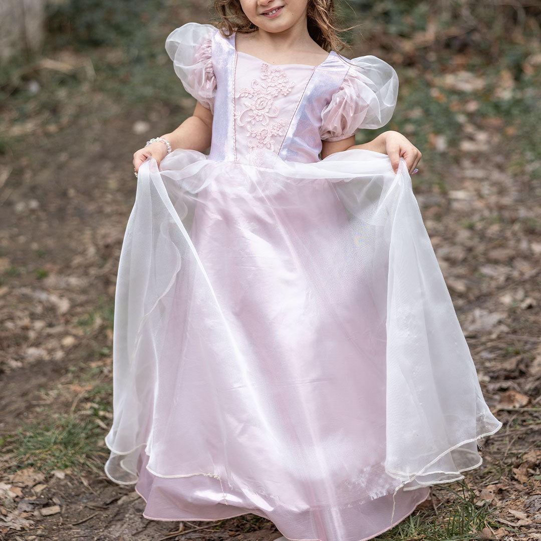 Een meisje draagt de roze prinsessen verkleedjurk en houdt de rok omhoog in een bosrijke omgeving.