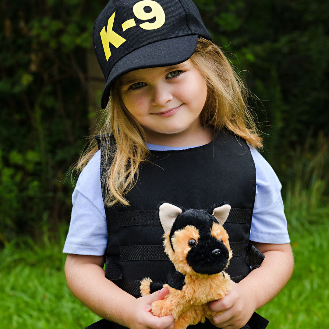 Een meisje draagt de great pretenders K-9 politieagent verkleedkleding en houdt de pluche hond vast.