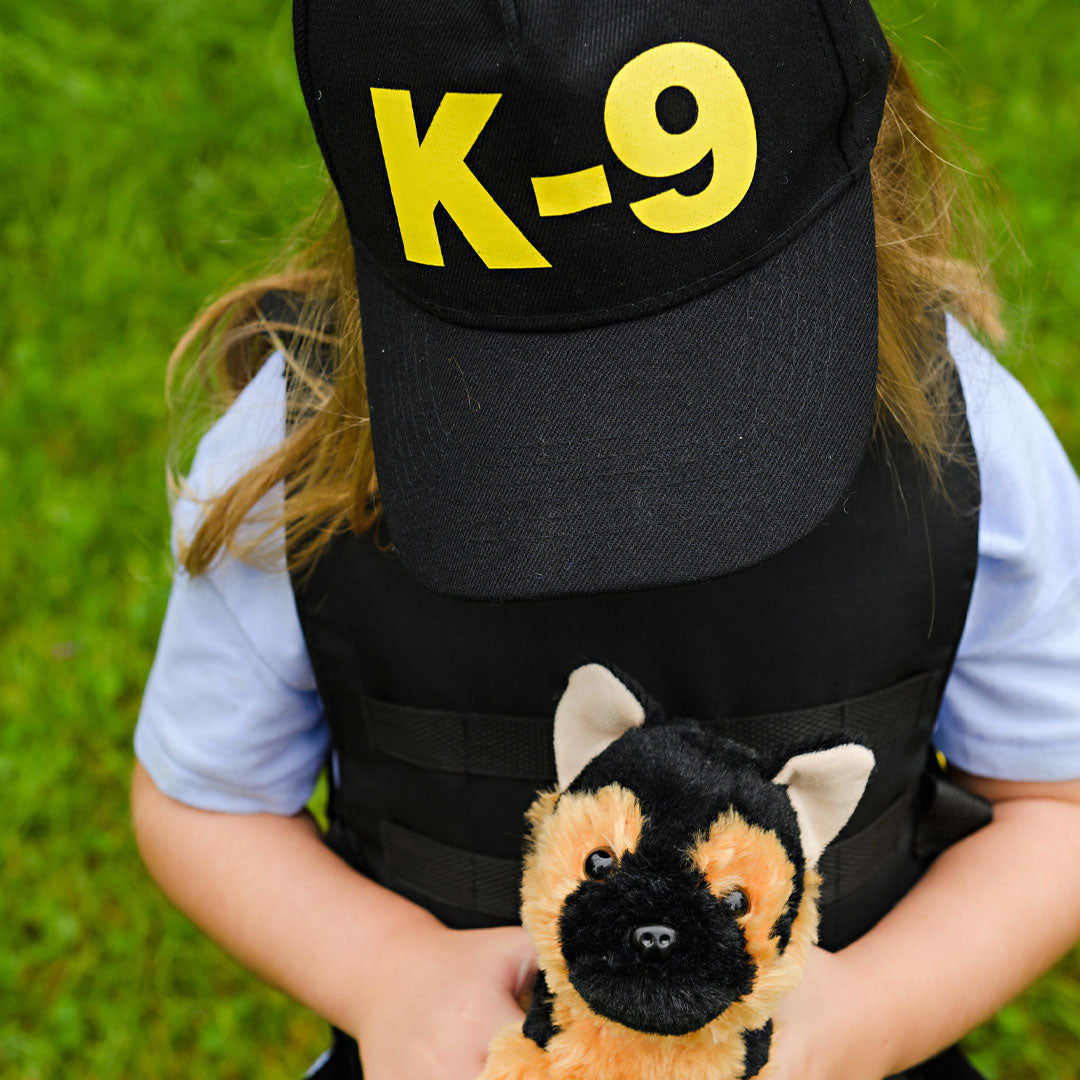Bovenaanzicht van een meisje in K-9 politieagent verkleedkleding dat de pluche Duitse herder vasthoudt.