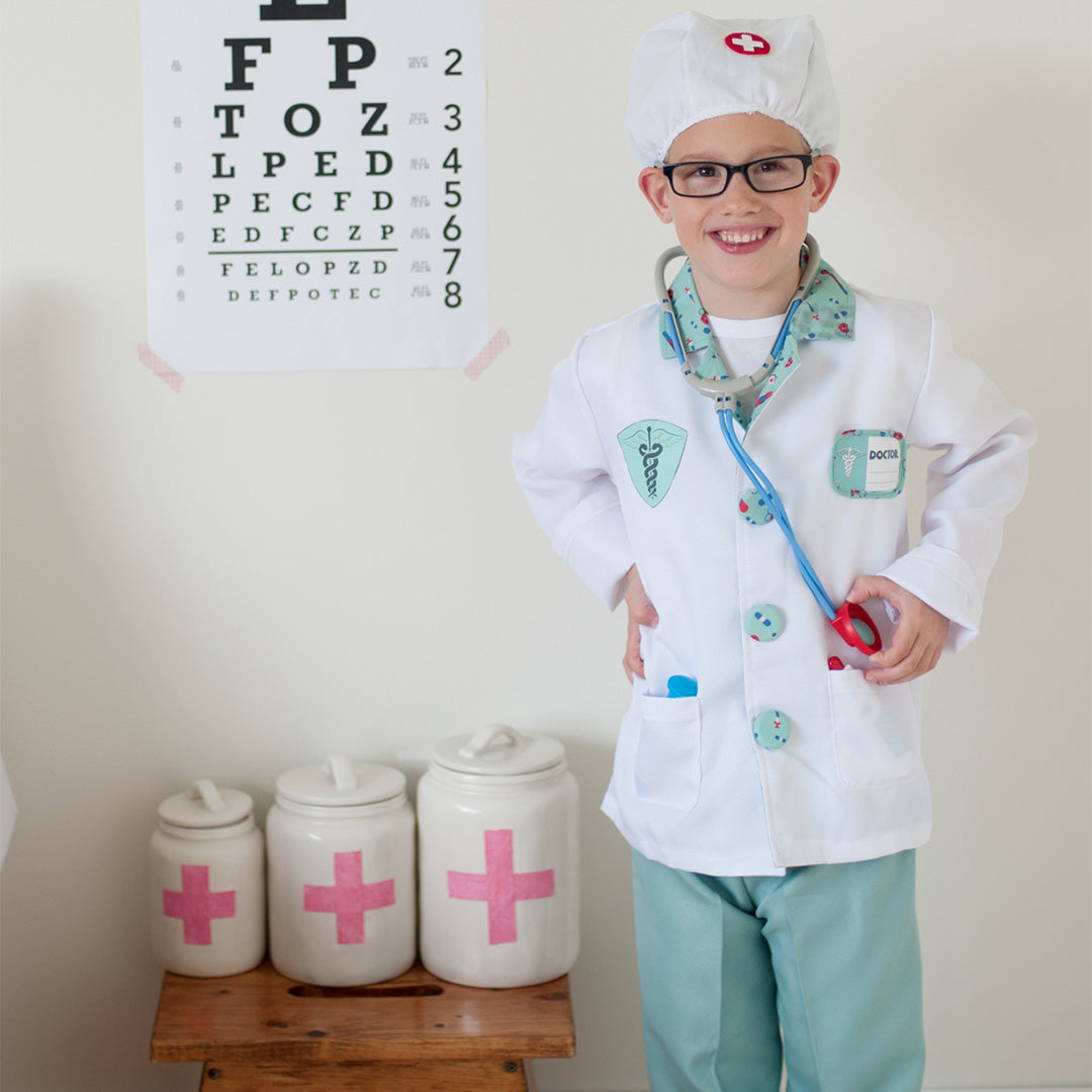 Lachende jongen in Great Pretenders dokter verkleedset met stethoscoop voor een oogtestkaart.
