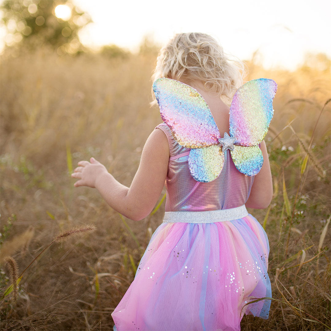 Een kind van achteren gezien draagt de great pretenders regenboog verkleedset met glimmende vleugels in een veld.