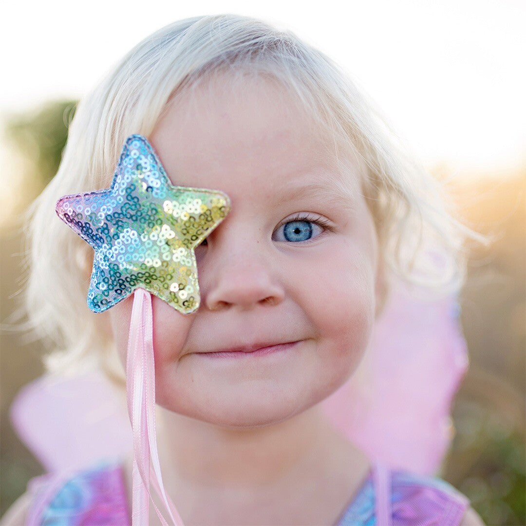 Close-up van een lachend kind met de great pretenders regenboog toverstaf voor haar oog.