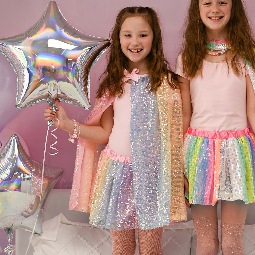 Twee lachende kinderen dragen great pretenders verkleedrokken met regenboog pailletten en bijpassende capes.