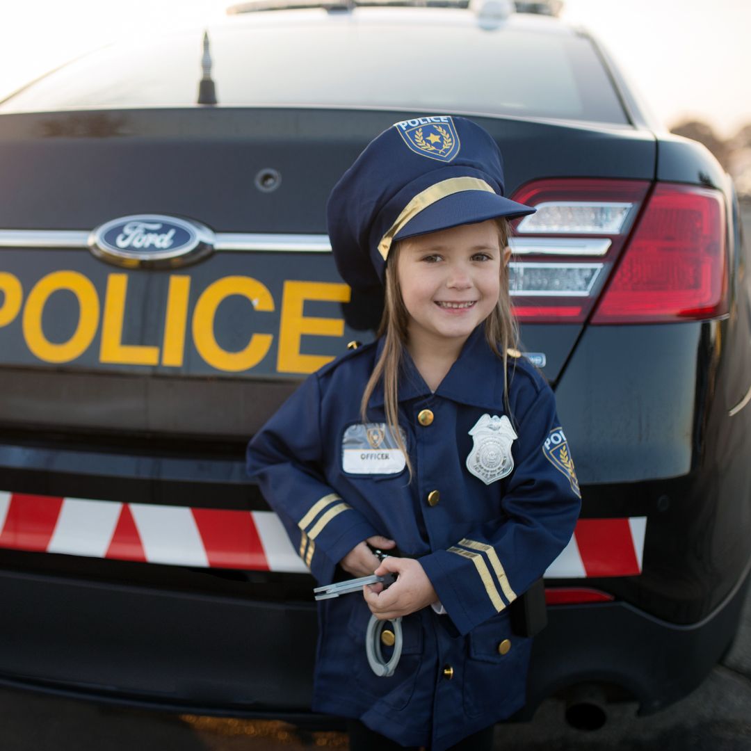 Lachend kind in politieagent verkleedset met handboeien voor een politieauto.