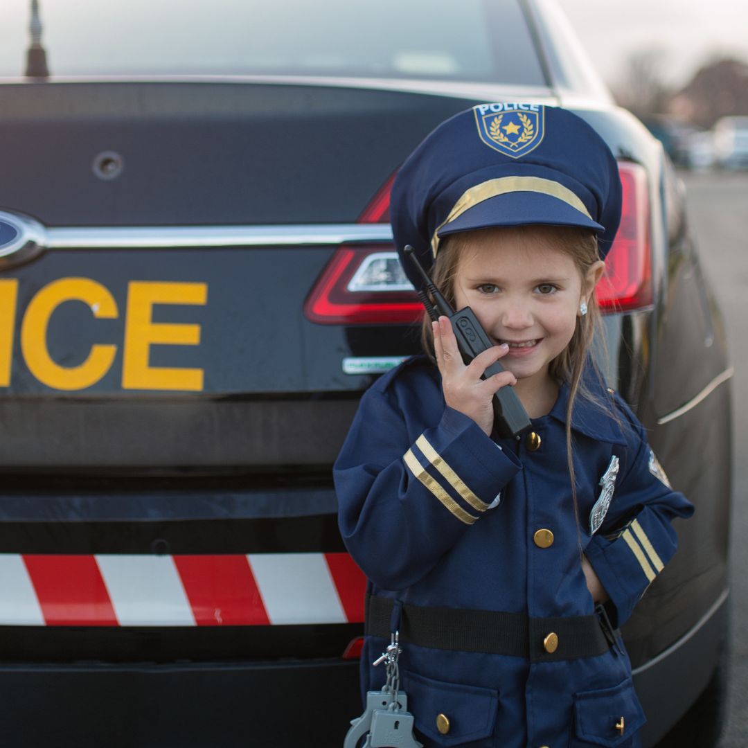 Lachend kind in politieagent verkleedset met walkie-talkie voor een politieauto.