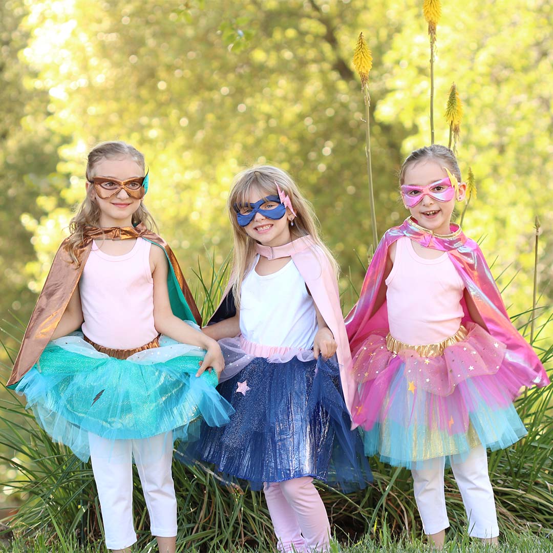 Drie lachende meisjes dragen verschillende Great Pretenders superhelden verkleedsets buiten.