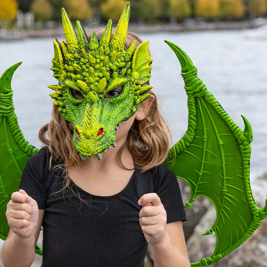 Close-up van een kind met Great Pretenders groene drakenvleugels en een groen drakenmasker.