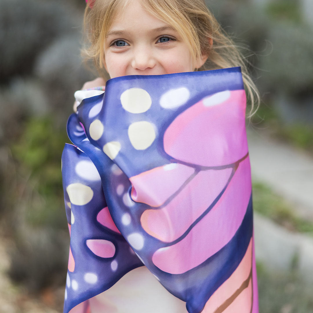 Close-up van een lachend meisje met de Great Pretenders vlindervleugels om haar heen gewikkeld.