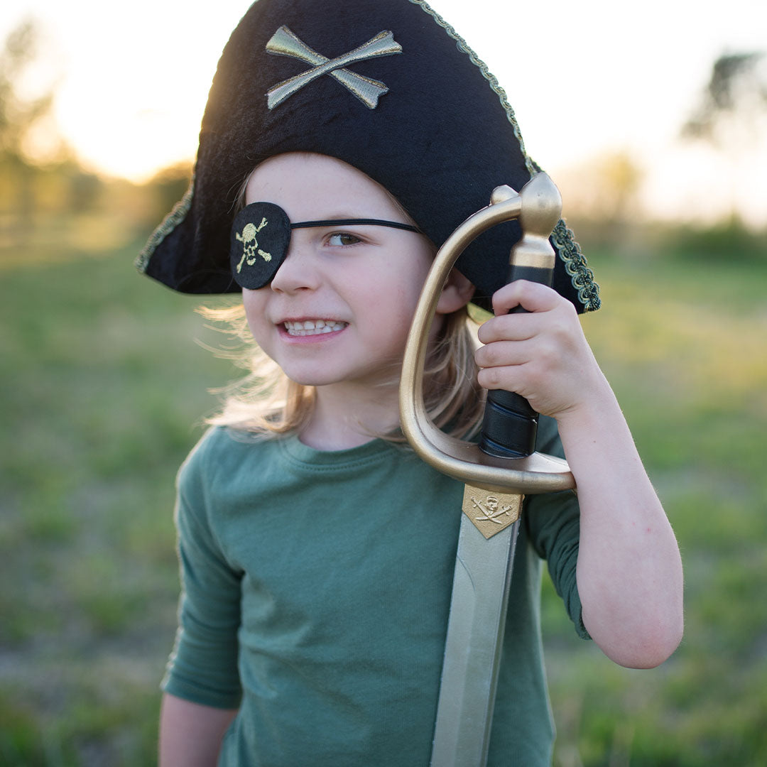 Kind met Great Pretenders piraten ooglapje en hoed, poserend met een speelgoedzwaard in een veld.