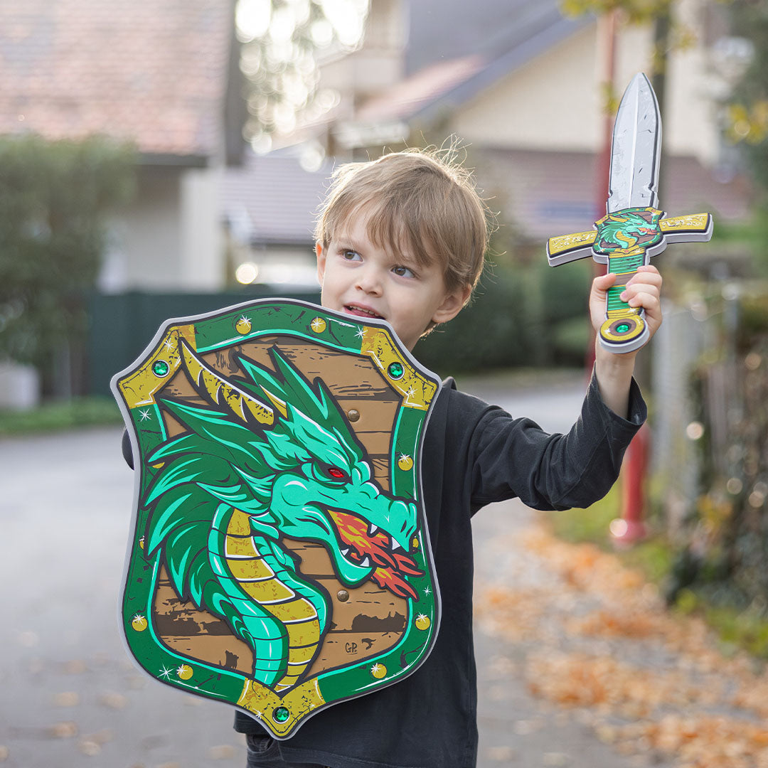 Een jongen kijkt opzij terwijl hij het Great Pretenders speelgoedschild met groene draak en een zwaard vasthoudt.