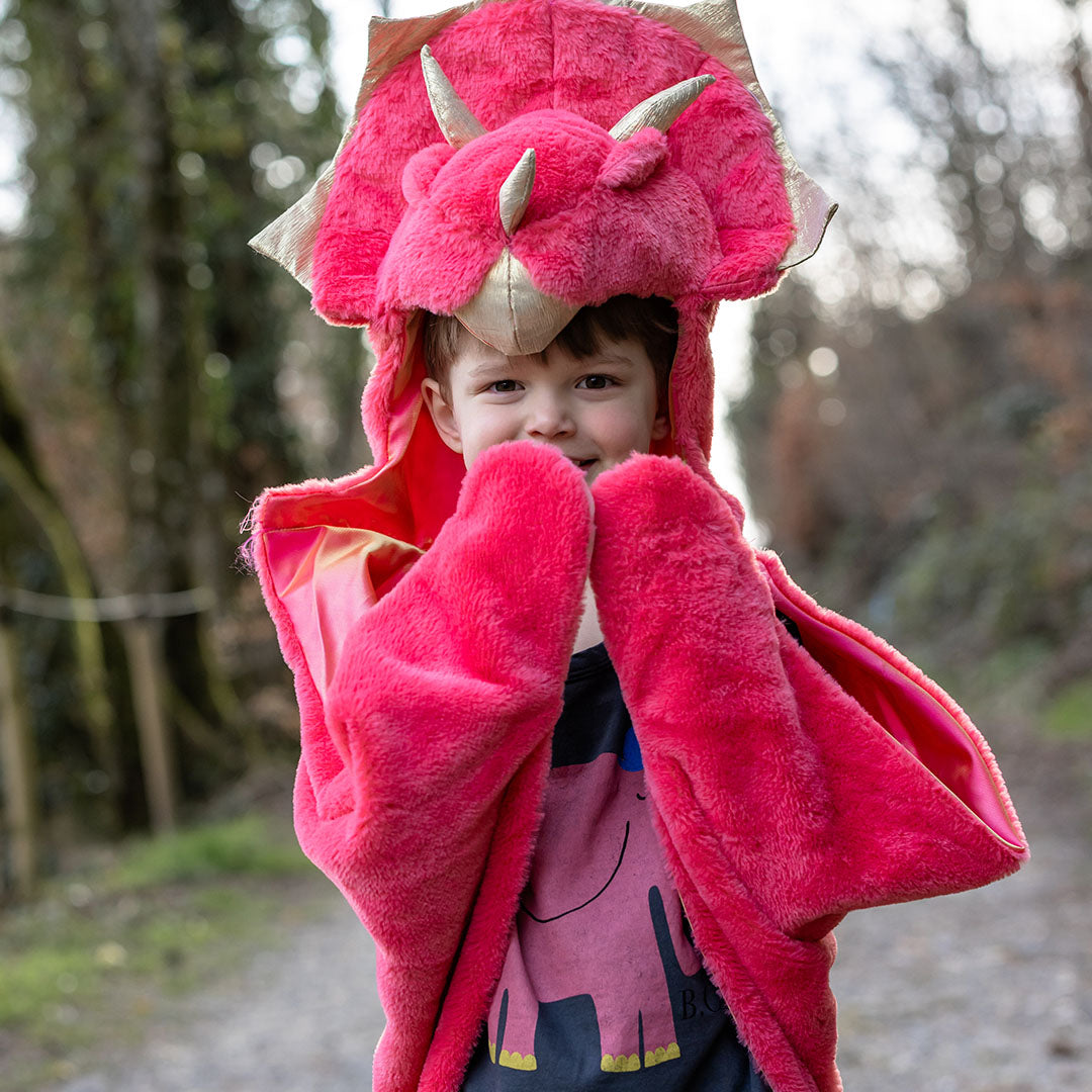 Een lachende jongen draagt de Great Pretenders rode triceratops verkleedcape buiten op een pad.