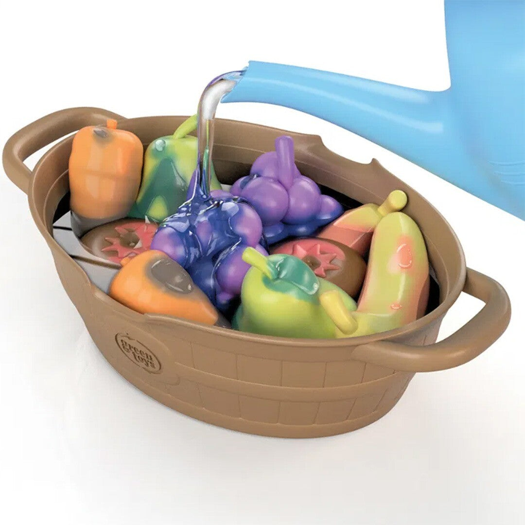 Water wordt uit een blauwe gieter in een bruine mand met plastic fruit en groenten speelgoed gegoten.
