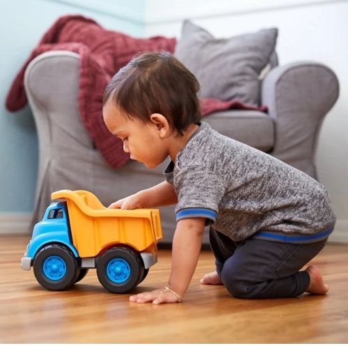 Een jong kind speelt op de houten vloer met een blauw-oranje speelgoedkiepwagen.