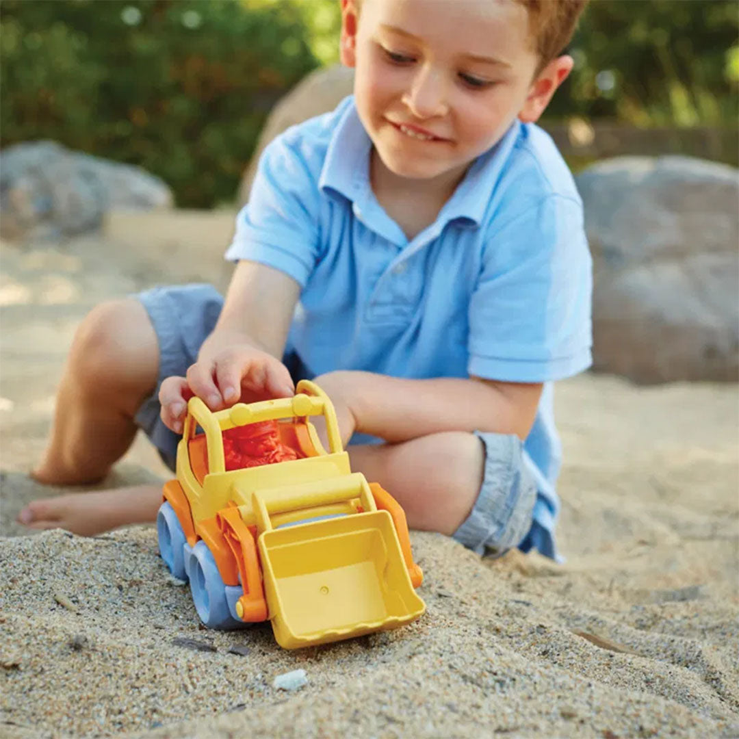 Een kind speelt zittend in het zand met de Green Toys oranje shovel.