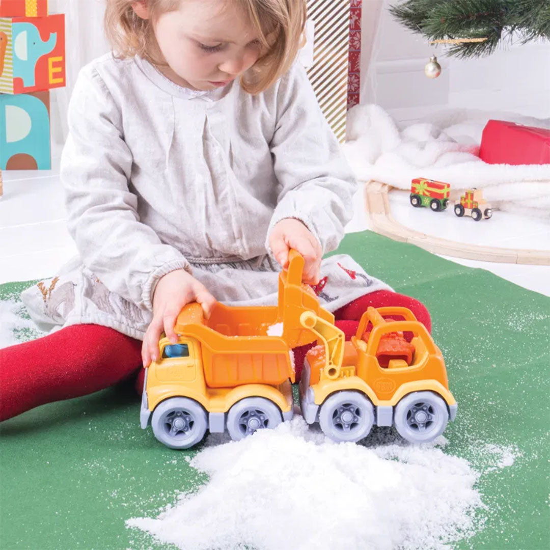 Een kind speelt met een Green Toys oranje shovel en kiepwagen in nepsneeuw.