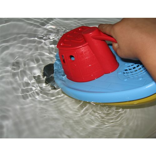 Een kinderhand houdt een rode en blauwe Green Toys sleepboot in het water.