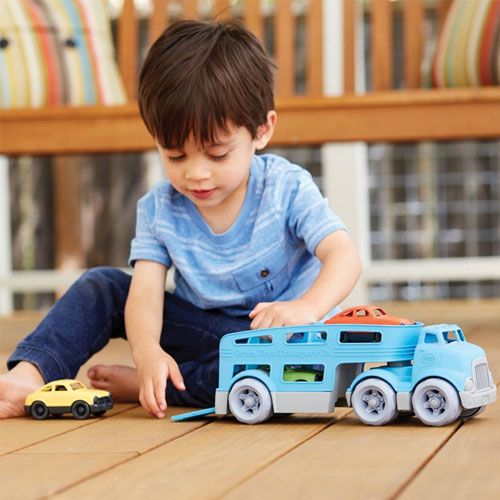 Een jongen speelt op een houten vloer met de Green Toys blauwe speelgoedvrachtwagen en een gele miniauto.