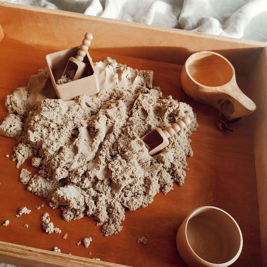 Bovenaanzicht van beige kinetisch zand met houten speelgoed in een houten bak.