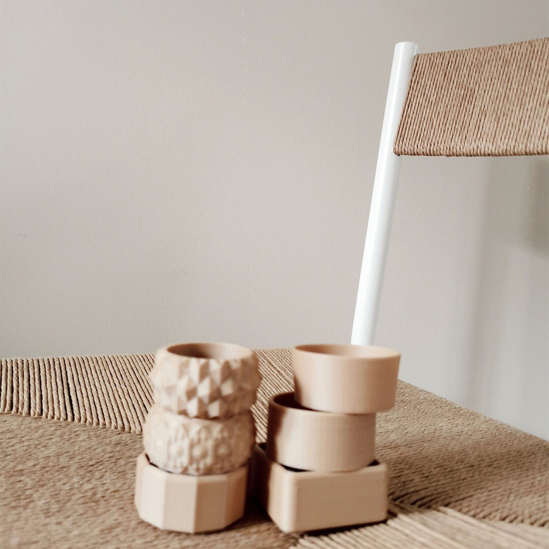 Een collectie grennn mini speelbakjes in beige kleur en verschillende vormen, gestapeld op een geweven stoel.