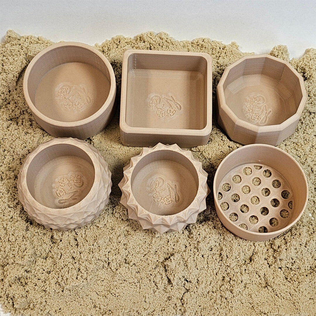 Zes grennn mini speelbakjes met zeef in beige kleur en diverse vormen, liggend in zand.