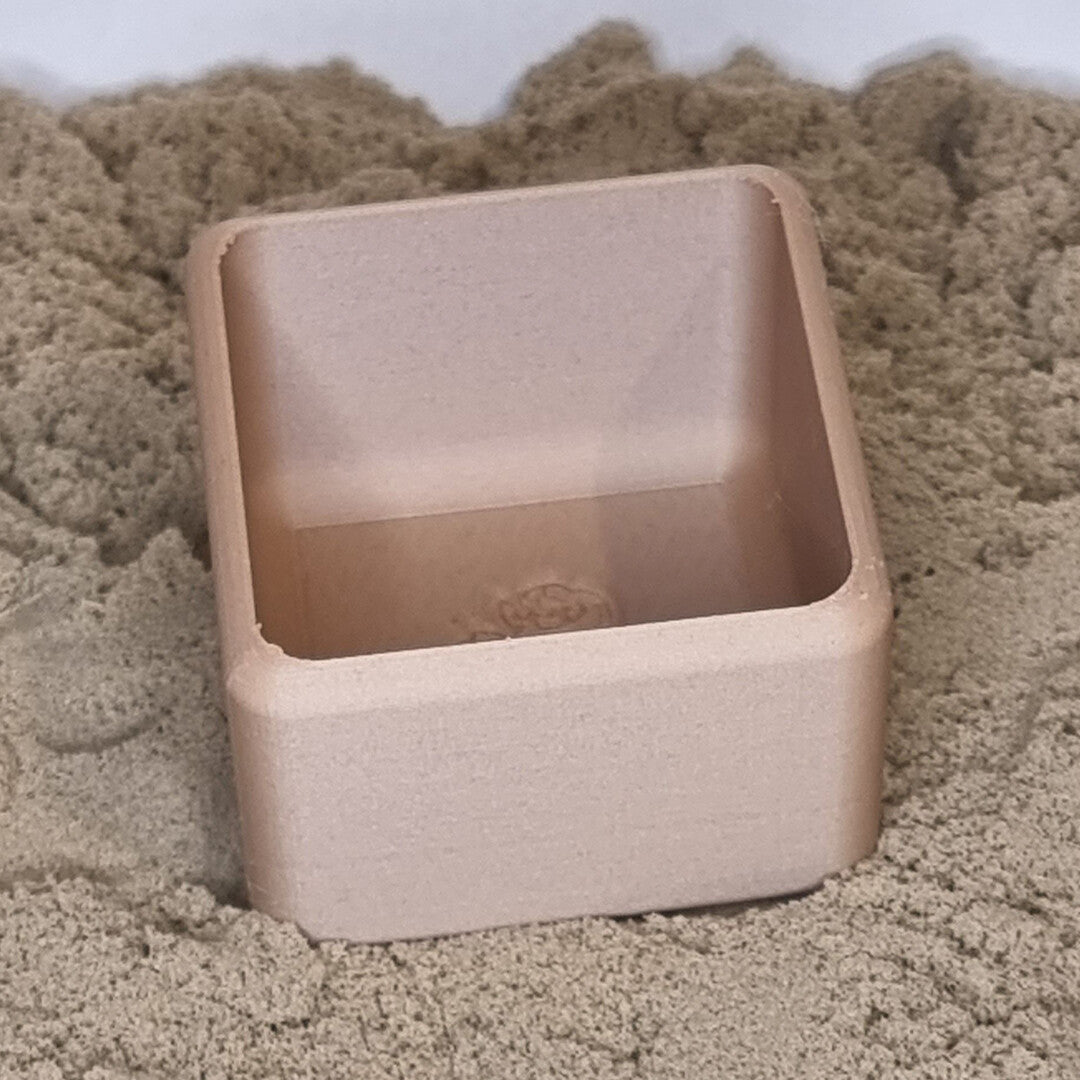 Een beige vierkant grennn speelbakje staat in het zand.