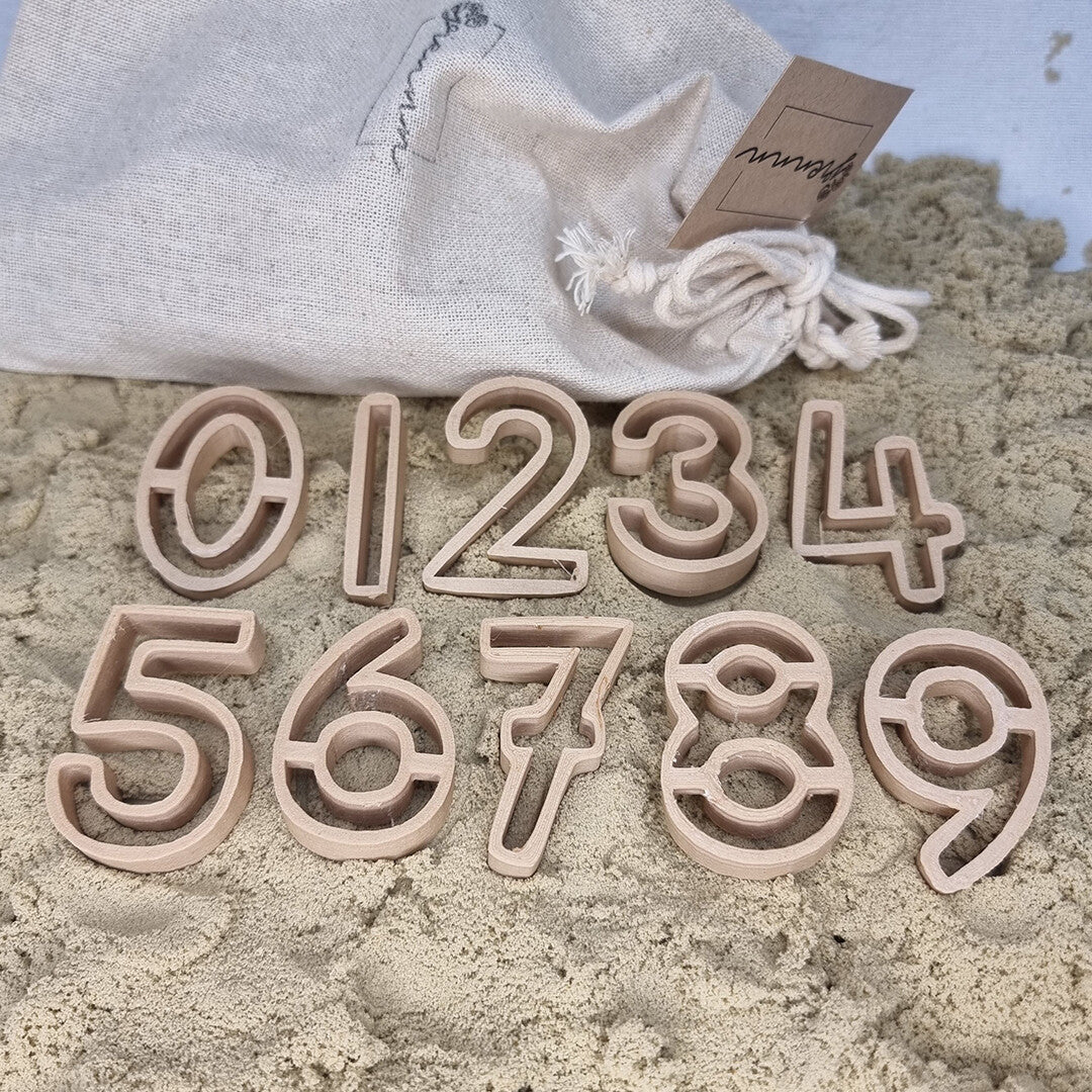 Grennn uitsteekvormen cijfers van 0 tot en met 9 liggen in het zand met een stoffen zak op de achtergrond.